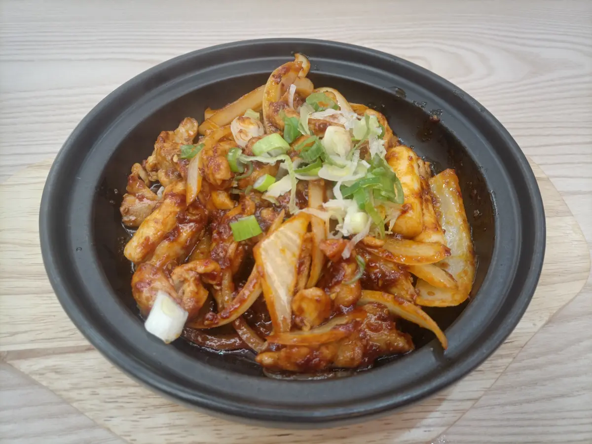 Dakgalbi spicy stir-fried chicken with sliced onions and green onions in a black stone pot on a wooden table