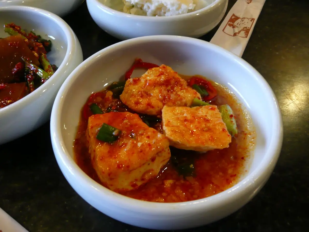 Braised tofu pieces in a spicy red sauce with scallions in a white bowl