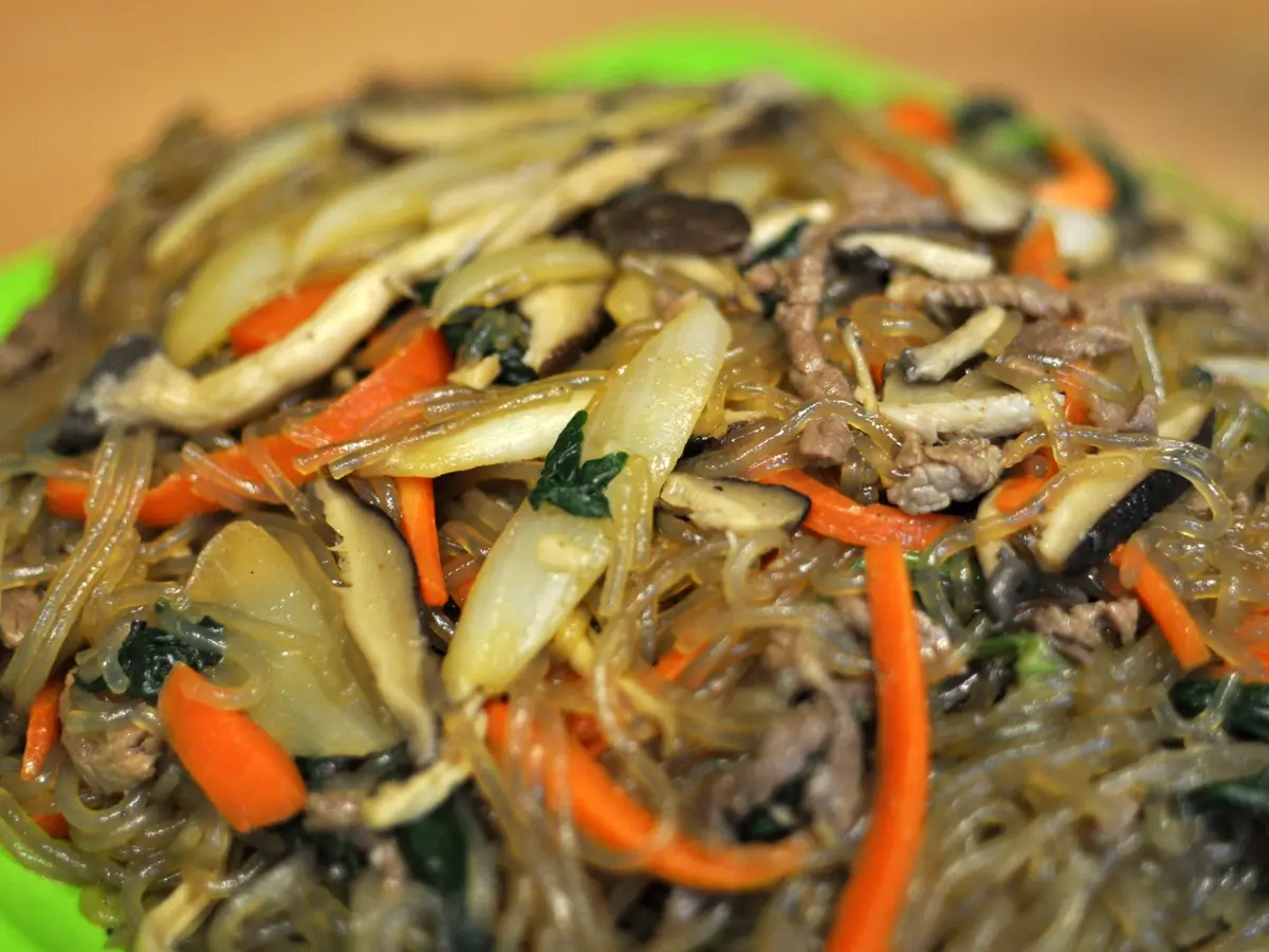 Japchae glass noodles tossed with sliced shiitake mushrooms, onion, carrot strips, spinach and bits of beef