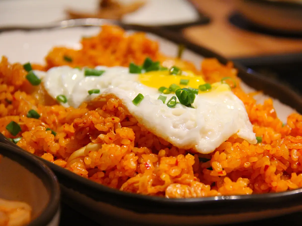 Close-up of red-orange kimchi fried rice topped with a sunny-side-up fried egg and sliced scallions