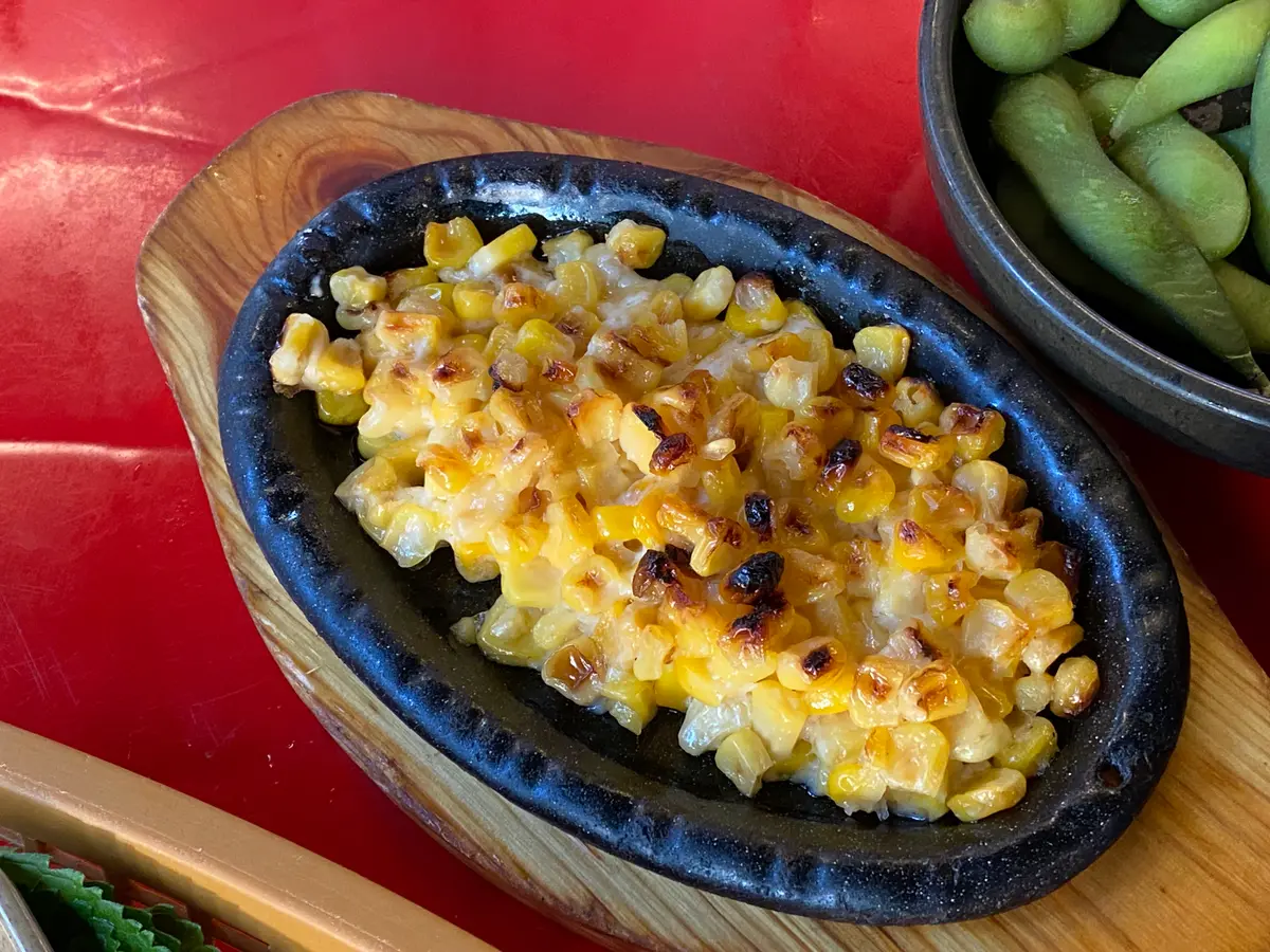 Korean corn cheese with melted, browned cheese on top served in a black oval dish on a wooden board