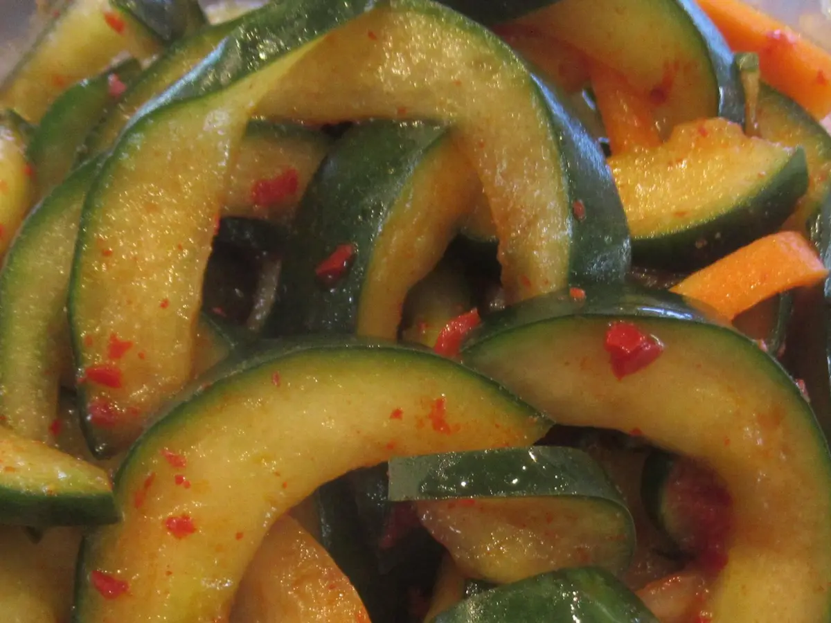 Close-up of oi muchim, Korean cucumber salad: glossy half-moon cucumber slices and carrot strips coated in red chili flakes