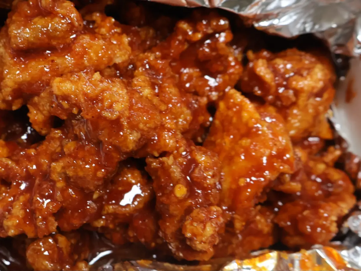 Crispy Korean fried chicken pieces coated in a glossy red-orange yangnyeom sauce, piled on crumpled aluminum foil