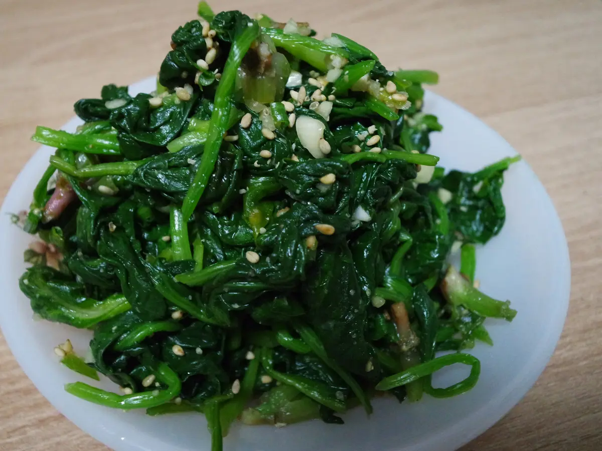 Korean seasoned spinach (sigeumchi namul) topped with toasted sesame seeds and minced garlic on a white plate
