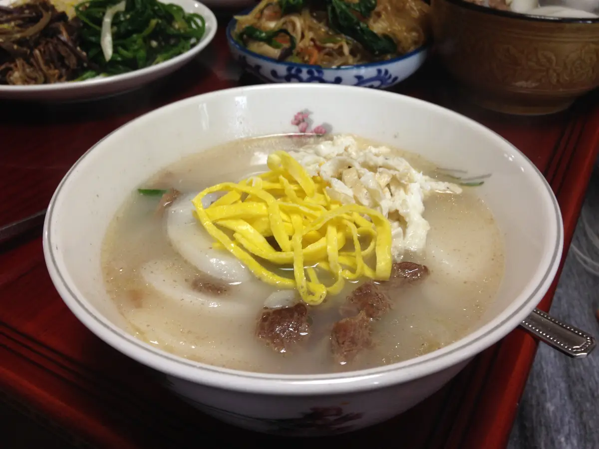 Tteokguk Korean rice cake soup with sliced rice cakes, beef and yellow and white egg strips in a white bowl